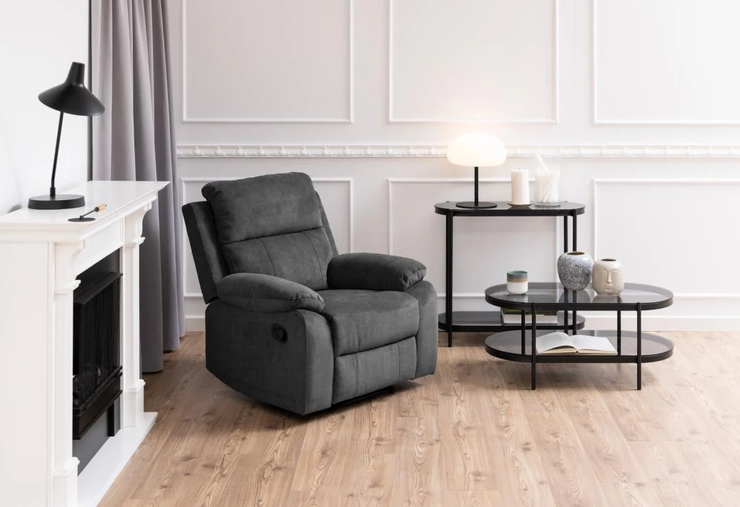 Een moderne woonkamer met een donkergrijze fauteuil, een Salontafel Zwart, Grijs 50 x 42 CM Rond van kunststof, gestyled met lampen, boeken, vazen, houten vloeren, wit gelambriseerde muren en een gordijn bij de open haard.