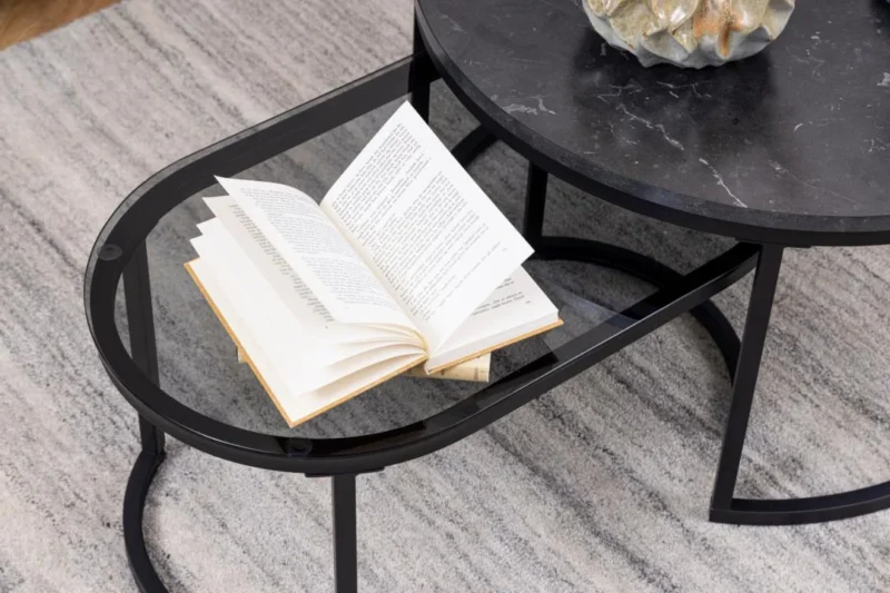 Een open boek ligt op de salontafel van Salontafel Rookglas, Zwart Rond Kunststof, met een grijs gestructureerd tapijt eronder. De pagina's van het boek zijn licht gekruld.