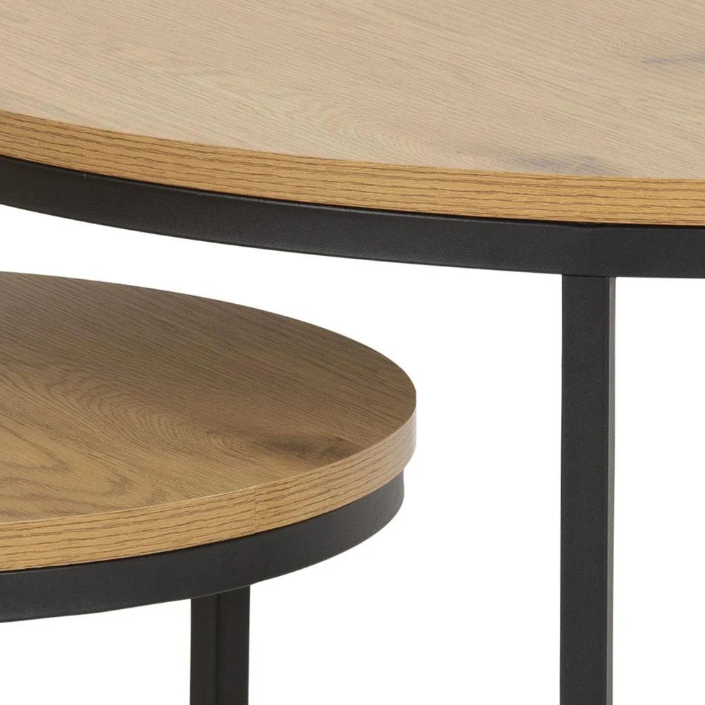 De Salontafel Rond Kunststof bestaat uit twee ronde, in elkaar geschoven tafels met bladen met licht houteffect en zwarte metalen poten, die van dichtbij worden getoond om het overlappende ontwerp en de contrasterende materialen te benadrukken.