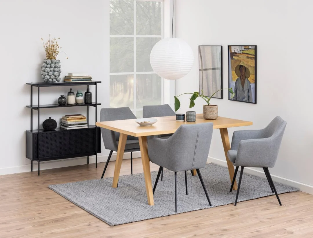 Een moderne eetkamer met de Angus boekenkast, een houten tafel, vier grijs gestoffeerde stoelen, een grijs vloerkleed en een zwart dressoir. Ingelijste kunst siert de witte muren terwijl natuurlijk licht binnenstroomt door een groot raam.