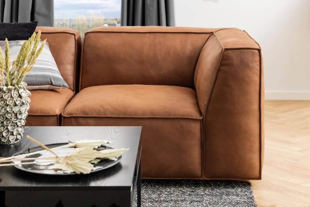 Een moderne woonkamer met een bruine leren bank, de Salontafel Zwart 80 x 40 CM Vierkant met een kunststof opbergvak en decoratief middenstuk, plus een gestreept kussen, vloerkleed en grijze gordijnen over het raam op de achtergrond.