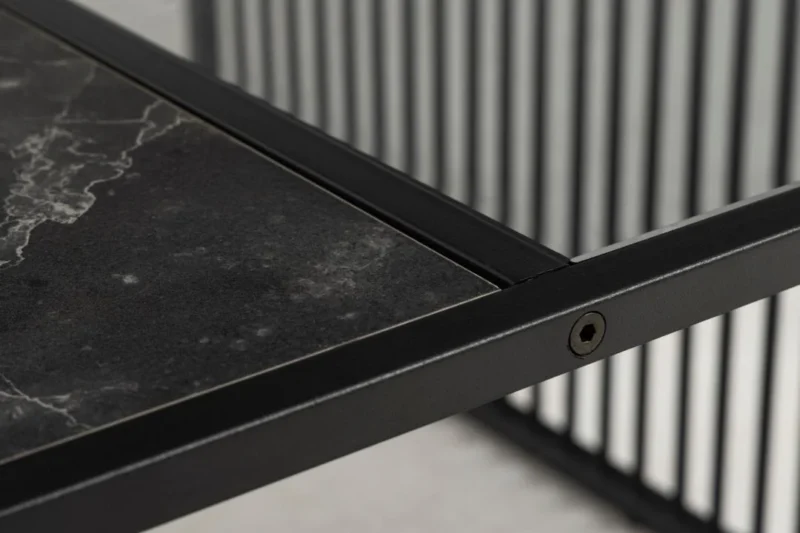 Close-up van de Salontafel Rookglas, Zwart 80 x 40 CM met een vierkant tafelblad van rookglas en een zwart metalen frame. Strakke lijnen en verticale metalen latten op de achtergrond benadrukken het moderne, minimalistische, industriële ontwerp.
