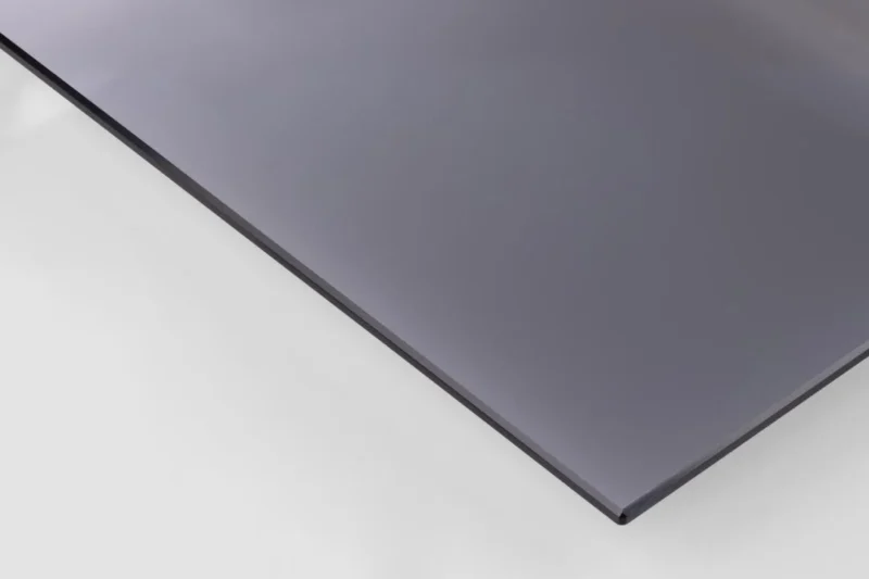 Een close-up van Salontafel Zwart, Grijs 80 CM Rond Staal toont het slanke, donkere ronde tafelblad met gladde stalen randen dat op een wit oppervlak rust. Dit accentueert de elegante afwerking en de moderne transparante stijl.