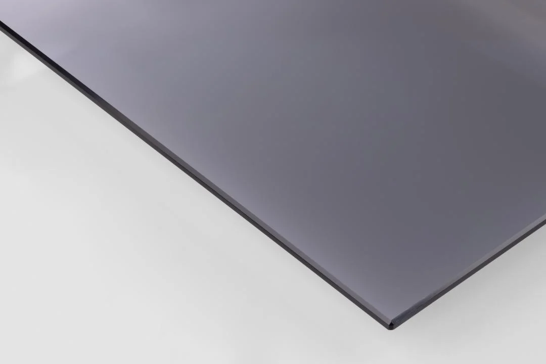 Een close-up van Salontafel Zwart, Grijs 80 CM Rond Staal toont het slanke, donkere ronde tafelblad met gladde stalen randen dat op een wit oppervlak rust. Dit accentueert de elegante afwerking en de moderne transparante stijl.