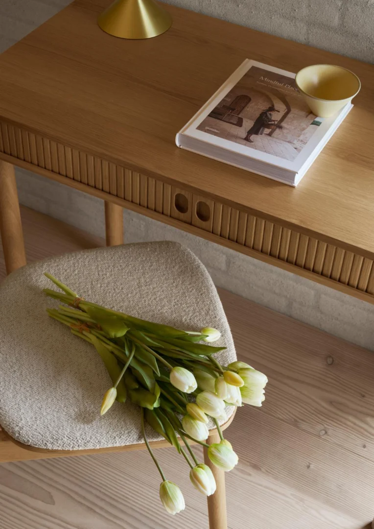 Eiken bureau Langley 100x50. Bureau met rolluik opbergruimte, boek, en tulpen op een stoel.
