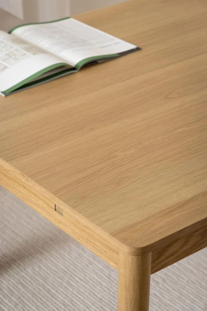 De Eettafel Nieuwe Sfeer 100 x 75 CM Rond, gemaakt van eikenhout, ligt op een vloerkleed met textuur en een open boek rustend bij de ronde rand.