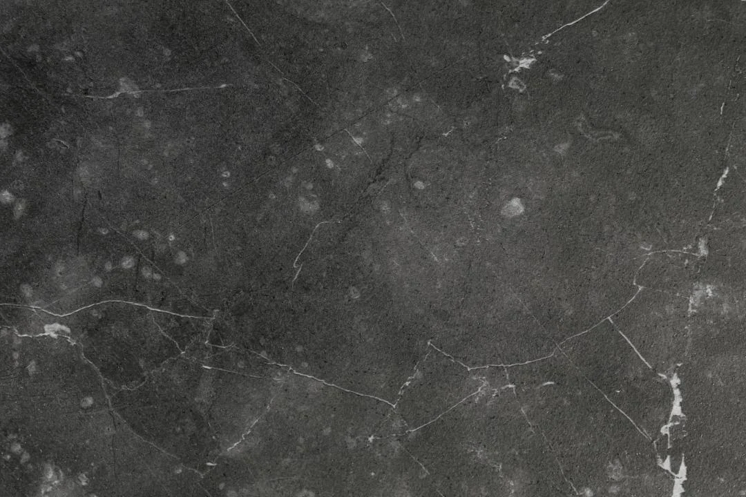 Close-up van een matzwarte industriële achtergrond met witte aders en vlekken. Het oppervlak heeft een ruwe, marmerachtige textuur.