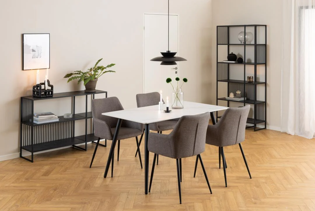 Eetkamer met witte tafel, grijze stoelen en een matzwarte metalen boekenkast. Lichte houten vloer en zachte belichting.