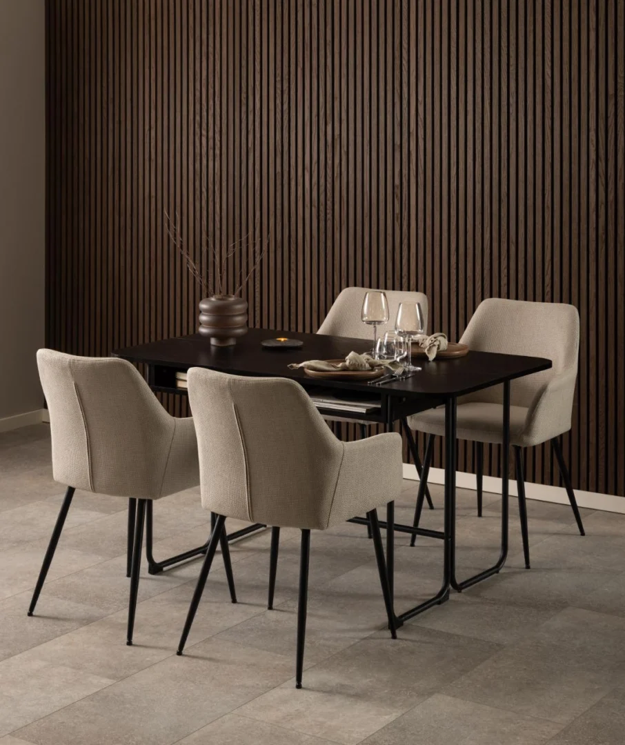 Een moderne eethoek met de Eettafel Nieuwe Sfeer 80 x 77 CM (rechthoekig MDF en staal), vier beige gestoffeerde stoelen met zwarte poten, twee wijnglazen, borden en een bruine vaas met droge takken bij verticale houten lattenwanden.