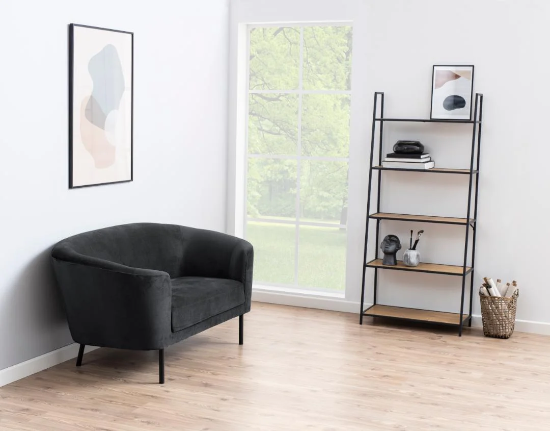Een minimalistische woonkamer met een zwarte loveseat, de Seaford boekenkast met houten planken met decoratie, een ingelijst abstract kunstwerk, een groot raam en een mand met opgerolde papieren op een lichte houten vloer.