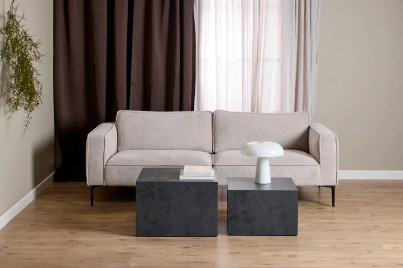 Een moderne woonkamer met een beige bank, een Salontafel Zwart 58 x 40 CM Vierkant Kunststof Nesting Set als salontafels, een witte paddestoellamp, boeken, bruine en witte gordijnen voor het raam, een hangende groene plant en een lichthouten vloer.