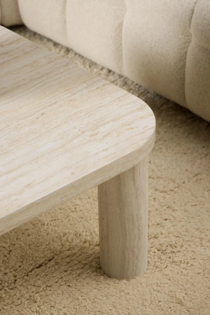 Een close-up van de Salontafel Beige 100 x 75 CM Rond Mdf salontafel met afgeronde hoeken en cilindrische poten, geplaatst op een beige getextureerd tapijt naast een crèmekleurige gestoffeerde sofa.