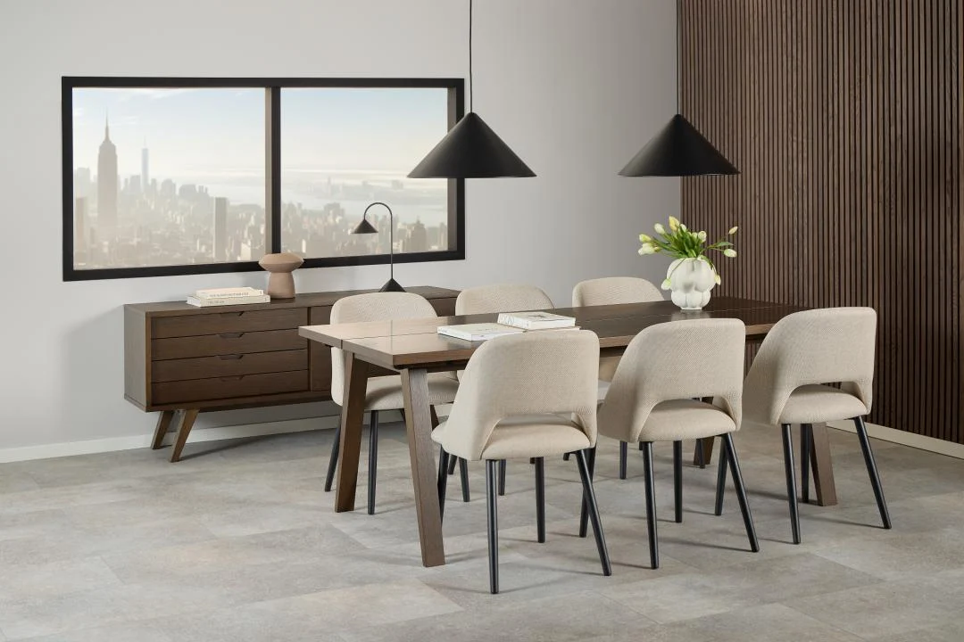 Een moderne eetkamer met de Eettafel Nieuwe Sfeer 200 x 95 CM rechthoekige eiken tafel, acht beige stoelen, een dressoir, twee zwarte hanglampen, een vaas met witte tulpen en een groot raam met uitzicht op de skyline van de stad in minimalistische neutrale tinten.