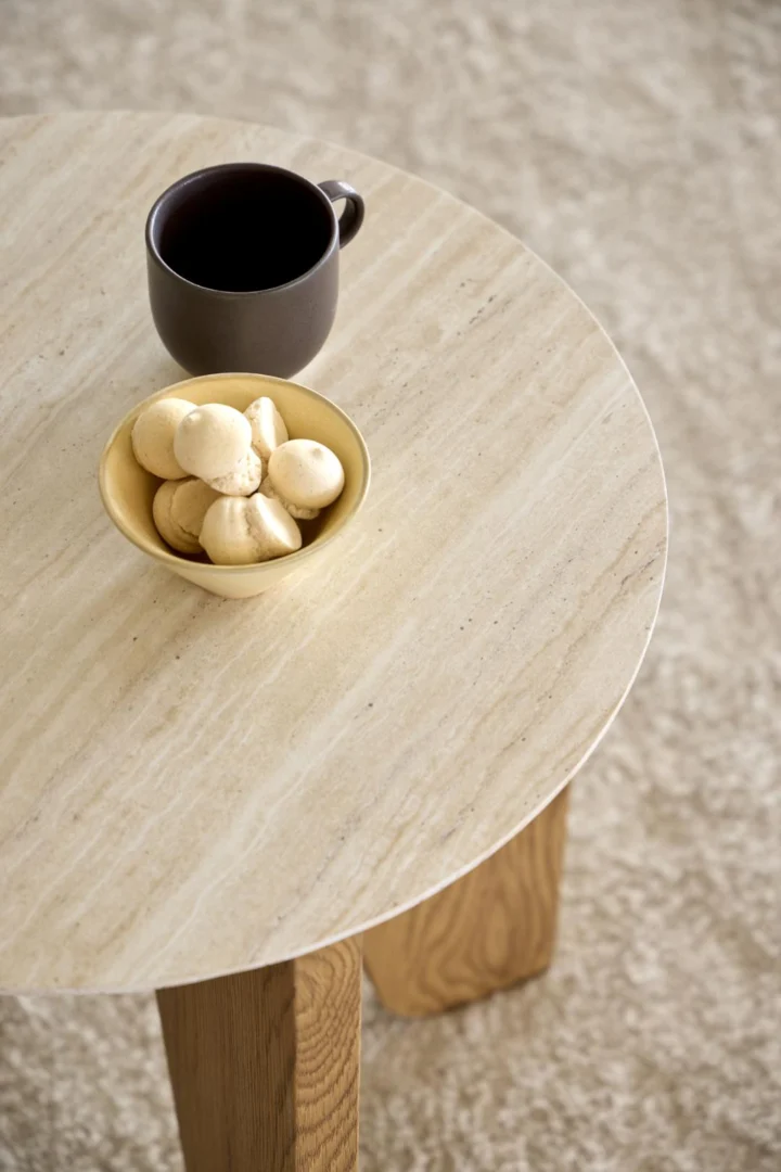 Een Bijzettafel Beige 50 CM Rond Kunststof ligt op een tapijt met een lichte structuur, met daarop een gele schaal koekjes en een donkere koffiemok.