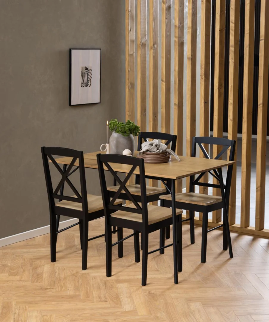 In een moderne eethoek staat de Eettafel Nieuwe Sfeer 80 x 75 CM Rond, een eikenhouten en stalen tafel, omringd door vier zwarte stoelen. De ruimte is voorzien van houten scheidingswanden, visgraatvloeren, een plant in potten en ingelijste muurkunst.