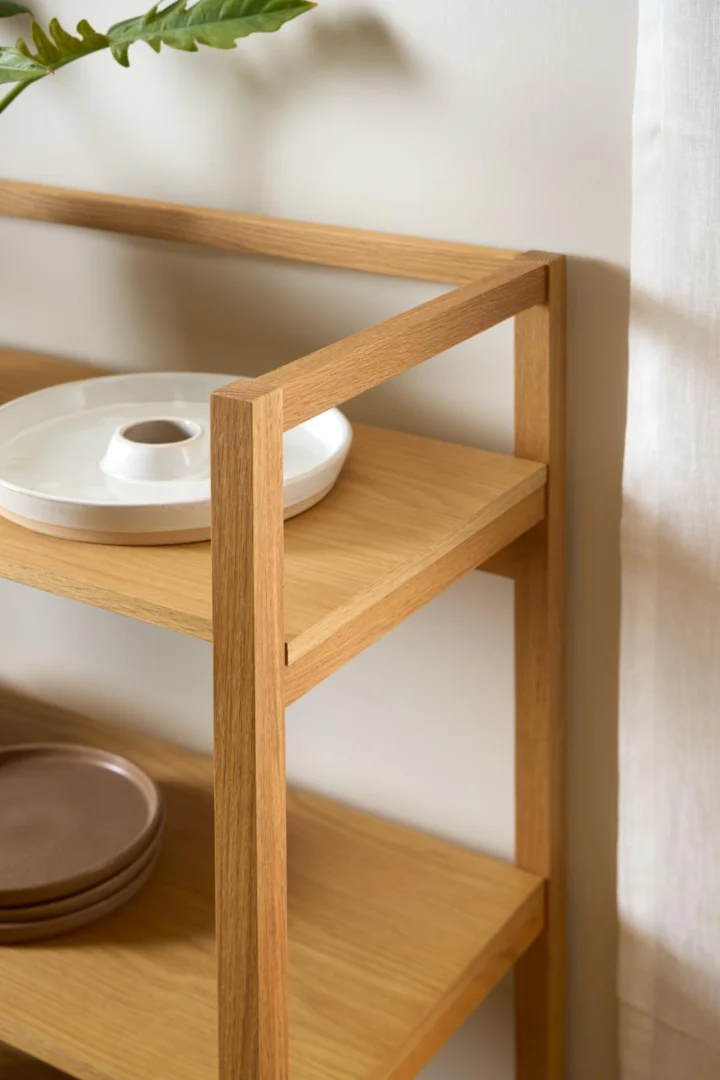 Detailopname van een naturel eikenfineer boekenkast met drie planken, zachte belichting, witte achtergrond en keramiek op de planken.