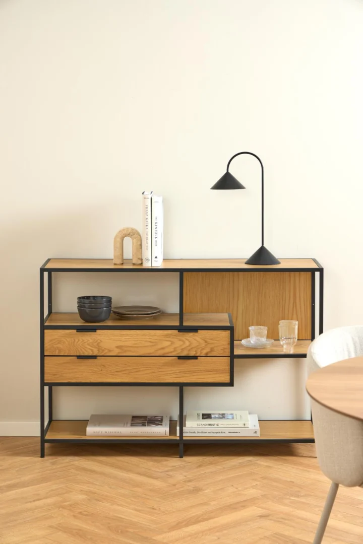 Asymmetrische boekenkast met eikenlook, stalen frame en twee lades. Neutrale achtergrond met zachte belichting. Modern design.