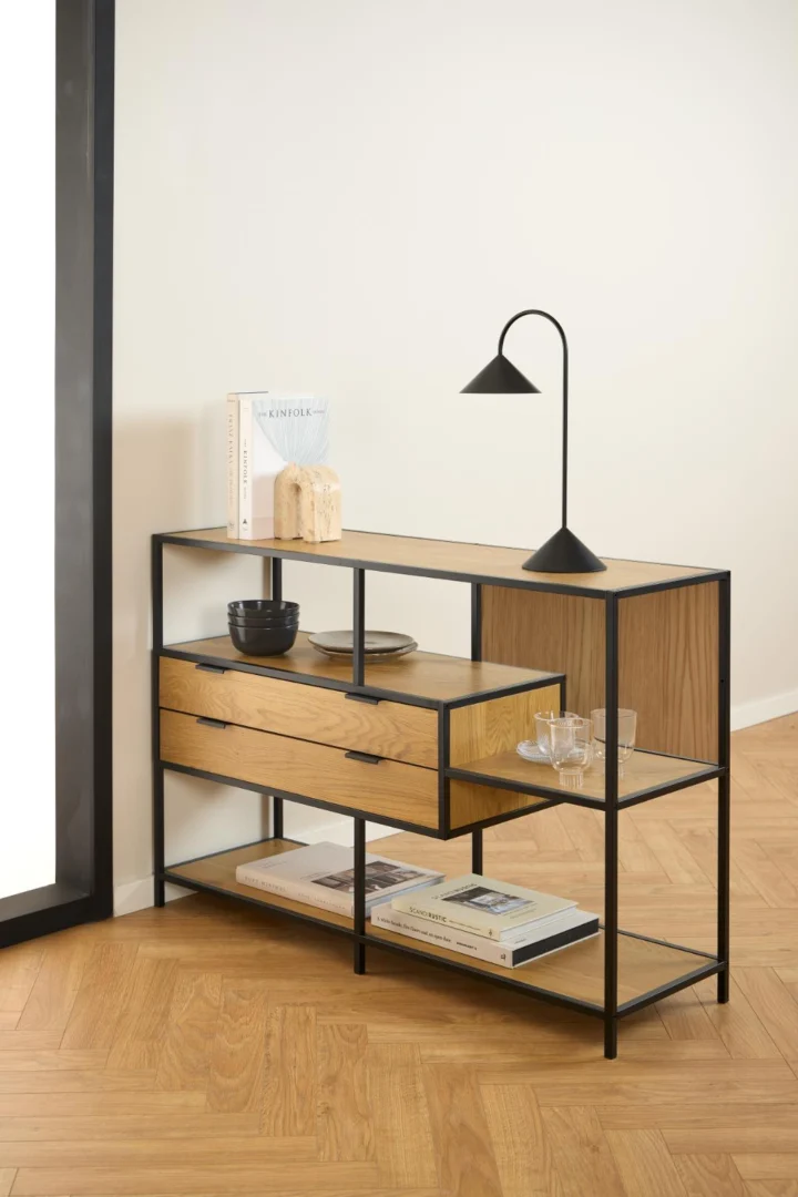 Asymmetrische boekenkast met eikenlook en zwart metalen frame, twee lades. Sfeervolle belichting, houten vloer in visgraatmotief.