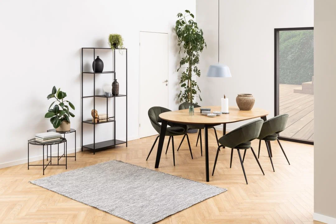 Moderne eetkamer met een Bijzettafel Zwart 42 CM Rond Kunststof, houten tafel, vier groene stoelen, gestreept vloerkleed, potplanten, open rekken met decor, een hanglamp en grote ramen die openen naar een houten terras.