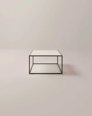 De Salontafel Zwart Klassiek Design is een minimalistische vierkante salontafel met een dun zwart metalen frame en een wit tafelblad tegen een effen lichtbeige achtergrond.