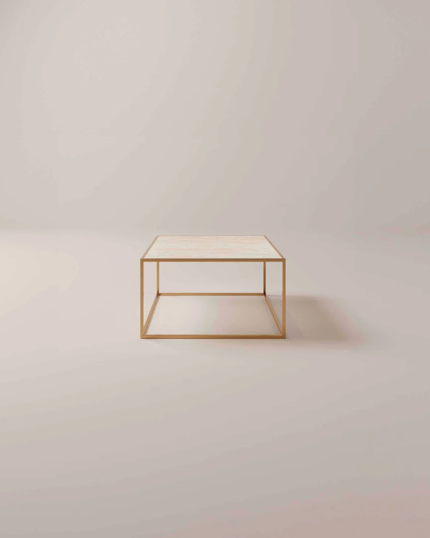 De Salontafel Messing, Roest heeft een minimalistisch ontwerp met een licht rechthoekig blad en een slank goud metalen frame, tegen een neutrale lichtbeige achtergrond.