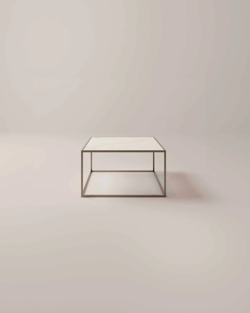 De Salontafel Brons is een minimalistische vierkante salontafel met een dun metalen frame en lichtgekleurd tafelblad, ideaal voor lege, zacht verlichte kamers met neutrale muren en vloeren.