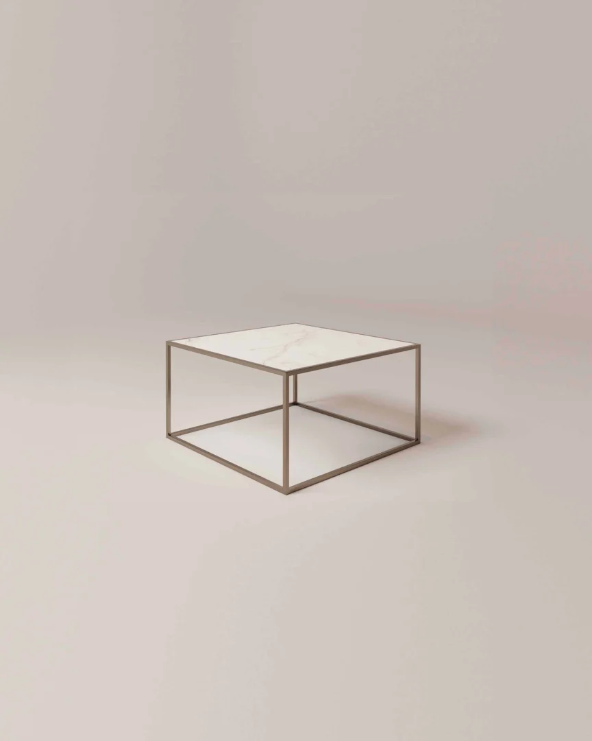 De Salontafel Brons is een minimalistische vierkante salontafel met een dun metalen frame en een wit marmeren blad tegen een effen lichtbeige achtergrond.