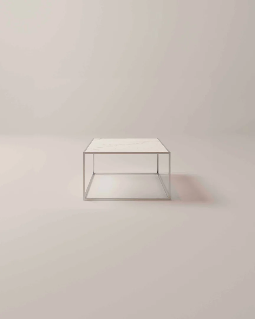De Salontafel Zilver Scandinavisch is een minimalistische vierkante tafel met een dun metalen frame en een wit blad tegen een effen, lichtgekleurde achtergrond.