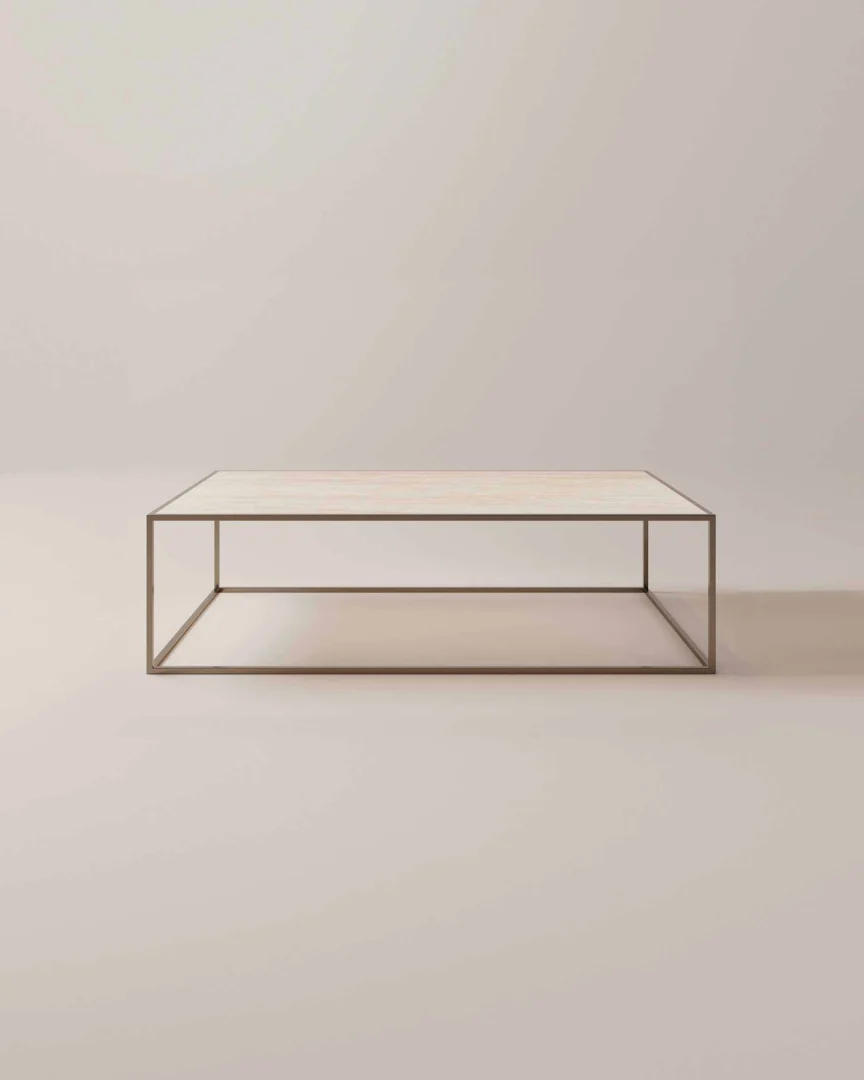 De Salontafel Brons Industrieel is een minimalistische rechthoekige salontafel met een dun metalen frame en een lichtgekleurd plat oppervlak tegen een effen, neutrale achtergrond.