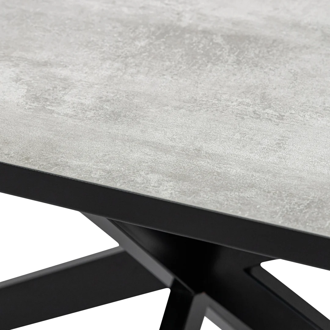 Close-up van de Stalux Eettafel 'Gijs' 180x100cm, met een gestructureerd lichtgrijs (beton) oppervlak en zwarte metalen poten met kruispatroon.