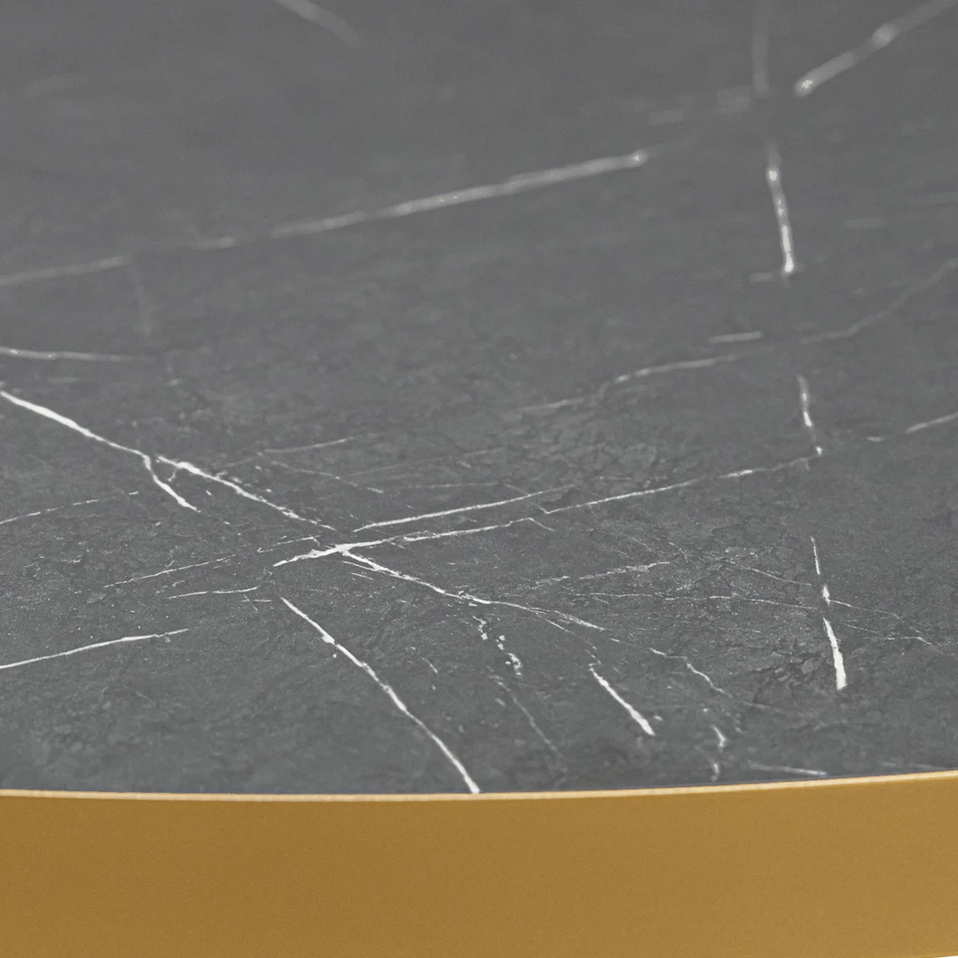 Een close-up van de Stalux Ronde eettafel 'Daan' (135cm) toont het ronde zwart marmeren tafelblad met witte adering en een matgouden rand.