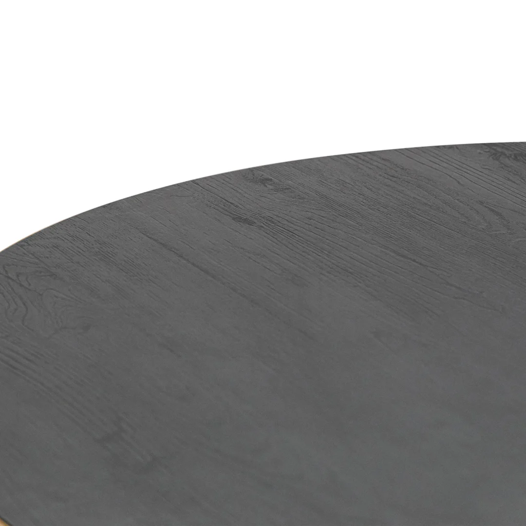 Close-up van de Stalux Ronde eettafel 'Daan' 135cm in goud/zwart eiken, waarop een deel van het ronde tafelblad te zien is met een donkere houtnerfstructuur die het grootste deel van het beeld vult.