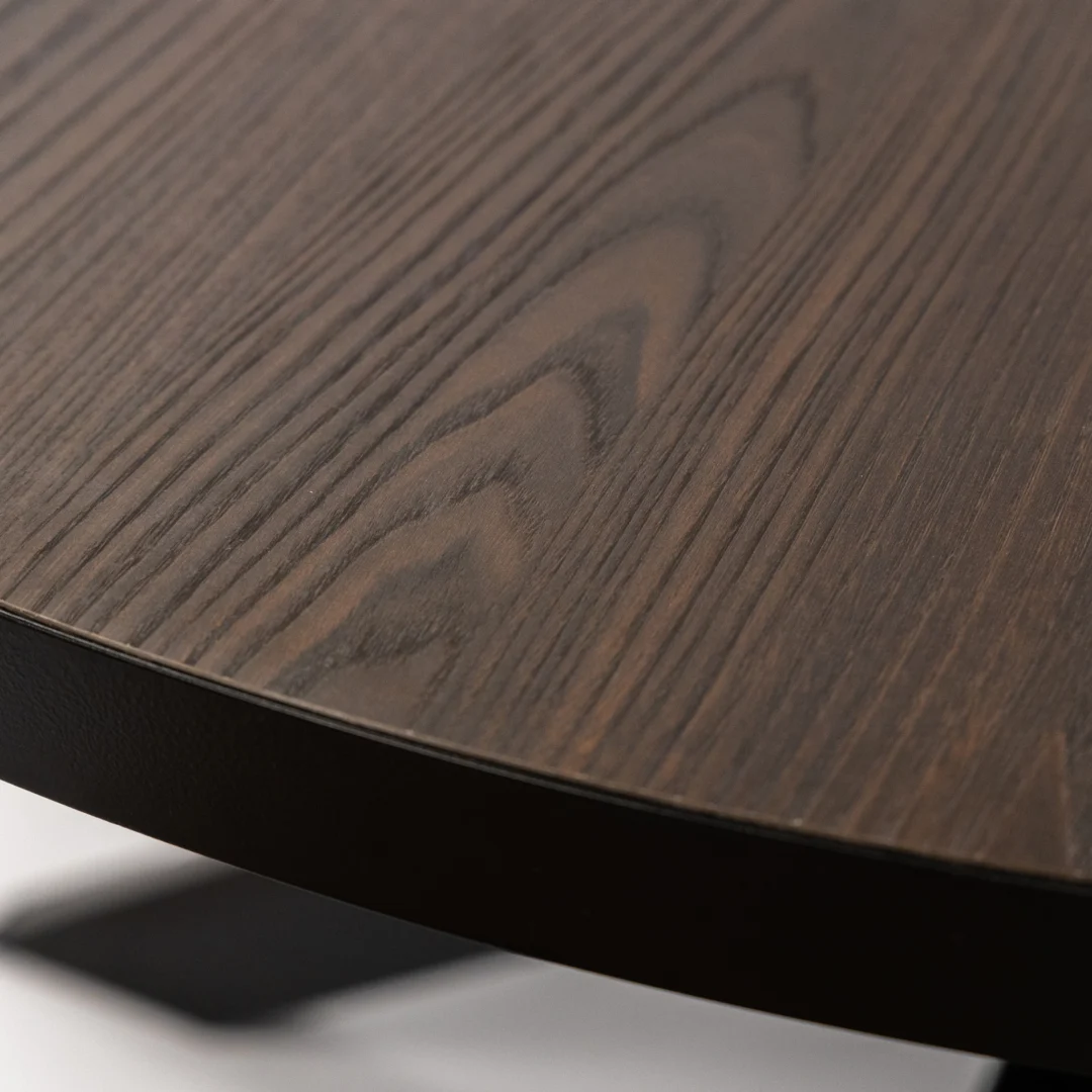 Close-up van de Stalux Ronde eettafel 'Daan' (148cm) met een donkerbruin houten tafelblad, zichtbare houtnerf, gladde afwerking en een zwart metalen onderstel. Kleur: zwart/bruin hout.