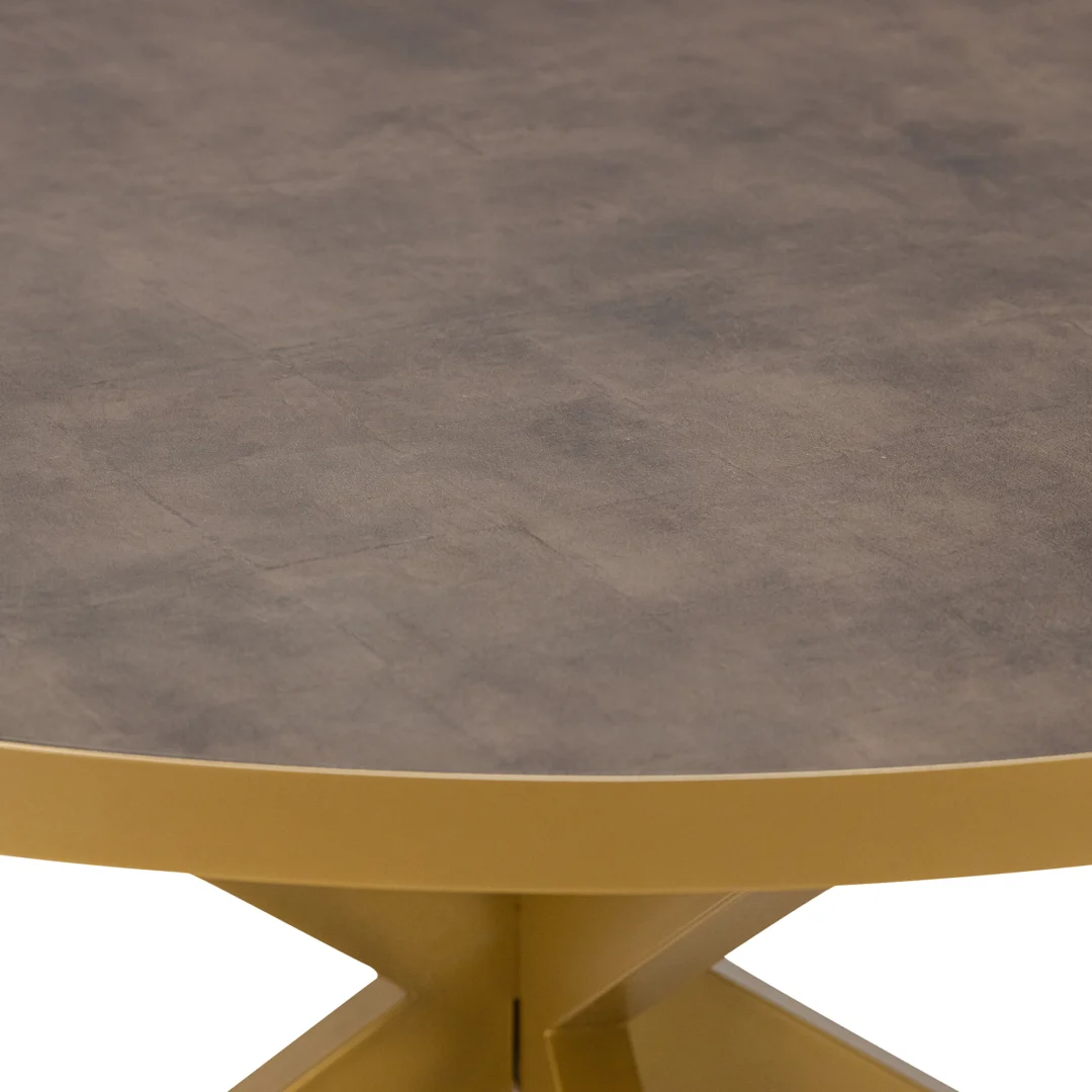 Een close-up van de Stalux Ronde eettafel 'Daan' 148cm toont het ronde tafelblad in lederlook bruin met een gouden metalen rand, ondersteund door een geometrische gouden voet.