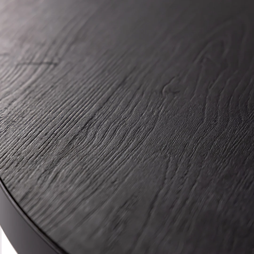 Close-up van de Stalux Ovale eettafel 'Mees' (210 x 100 cm) in zwart / zwart eiken, met de nadruk op het donkere houten oppervlak met zichtbare nerf en een gladde, afgeronde rand aan de linkerkant.