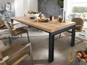 In een moderne eetkamer staat de Eettafel Herning Basano - 220x100 met bruine stoelen en borden erop. Daarachter maken een krijtbordmuur, historische kunstwerken, grote ramen met uitzicht op bomen en een mand met appels op de vloer het plaatje compleet.