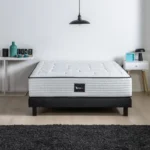 Wit matras met zwarte rand op een massief houten boxspringset. Neutrale achtergrond met zachte belichting. Modern en stevig.