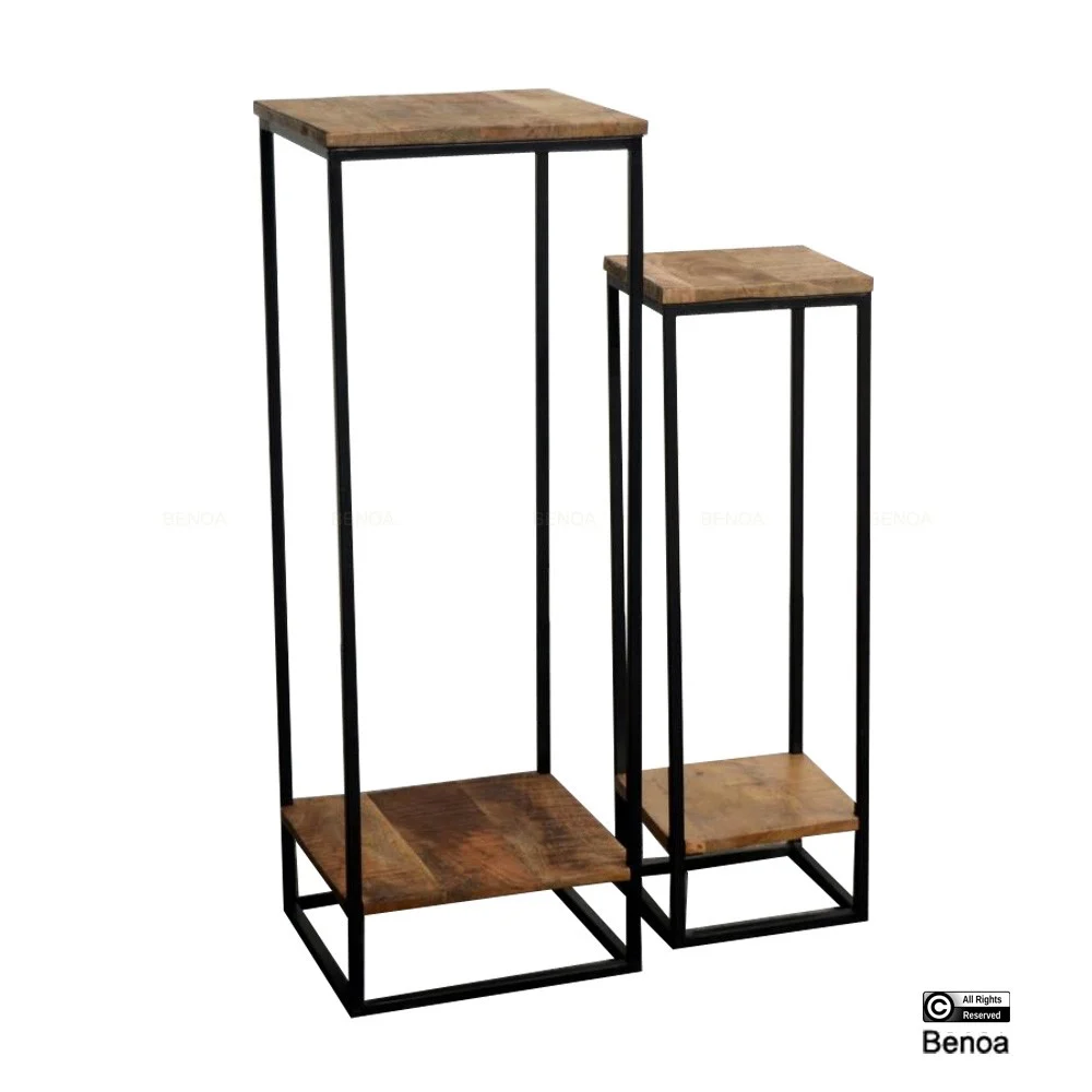 De Tafel voor Planten Set van 2 bestaat uit twee houten displaystandaards van verschillende hoogtes met zwarte metalen frames, elk met een vierkant houten blad, bijpassende onderste plank en slanke rechthoekige poten.