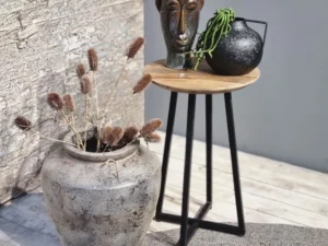 Een rustiek tafereel toont een grote stenen vaas met gedroogde planten naast de bijzettafel Ivy, die twee artistieke vazen toont - een in de vorm van een menselijk gezicht en een andere zwarte vaas met een groene plant.