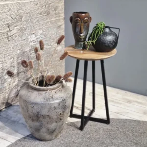 Een rustiek tafereel toont een grote stenen vaas met gedroogde planten naast de bijzettafel Ivy, die twee artistieke vazen toont - een in de vorm van een menselijk gezicht en een andere zwarte vaas met een groene plant.