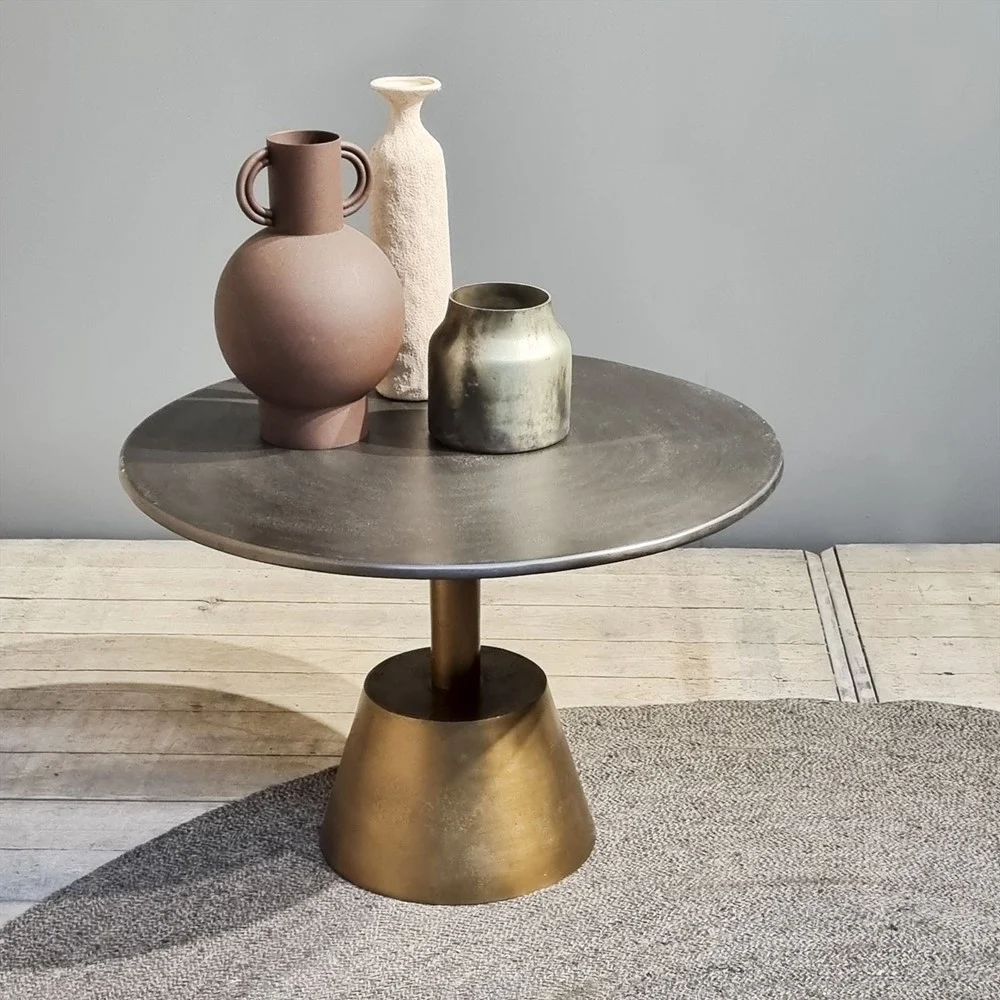 De Sidetable Kian Goud Zilver, met een koperen onderstel, toont drie aardegekleurde vazen - een ronde met handgrepen, een hoge met textuur en een korte met metallic - tegen een neutrale achtergrond en deels op een grijs vloerkleed.