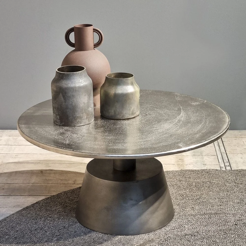 De Salontafel Zilver 82 x 82 CM Vierkant toont drie vazen - twee metalen en een bruine - tegen een neutrale muur en een vloerkleed met textuur op een lichte houten vloer.