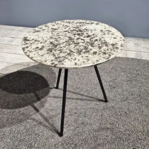 De Sidetable Koper Glas 38" heeft een klein, rond, steenachtig blad met drie dunne zwarte poten en staat op een grijs vloerkleed in een moderne minimalistische kamer.