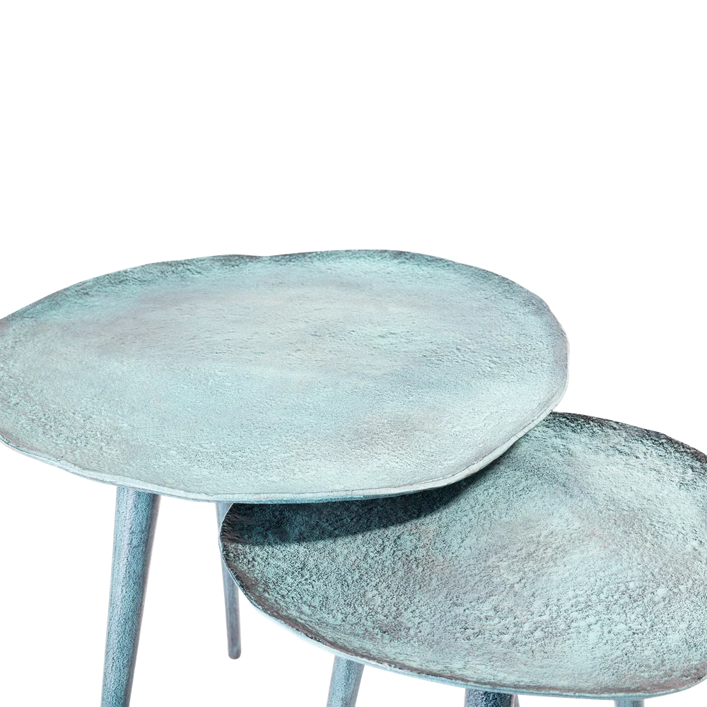 De Sidetable Blauw Patina 34,5 (set van 2) bestaat uit twee ronde, metalen bijzettafels met een gestructureerd turquoise oppervlak en elk drie poten, licht overlappend tegen een witte achtergrond.