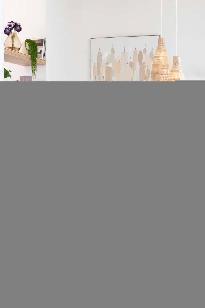 Een modern interieur met lichte muren, een Salontafel Grijs 60 x 53 CM Ovaal in mangohout, een gouden vaas met paarse bloemen, geweven hanglampen en abstracte kunstwerken in een eenvoudige lijst.