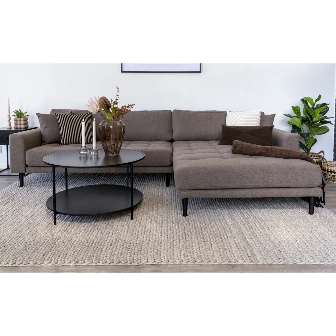 Een moderne woonkamer met een bruine sectionele bank, neutraal vloerkleed, potplanten en sierkussens is voorzien van Salontafel Zwart 80 x 45 CM Rond in spaanplaat, afgewerkt met kaarsen en een vaas voor een heldere, minimale look.