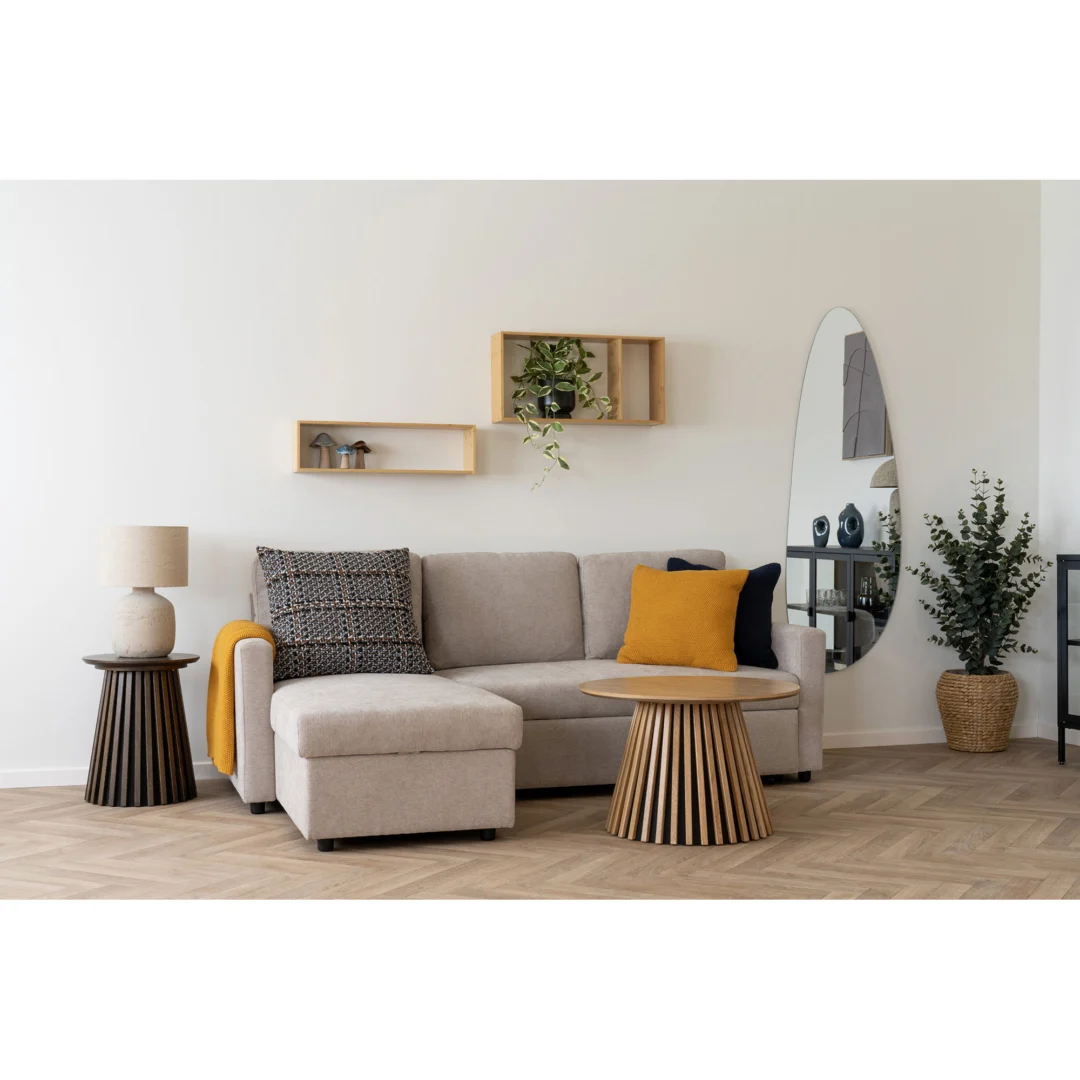Een moderne woonkamer met een lichtbeige sectionele bank, gele kussens en kussens met patroon, twee salontafels 70 x 45 CM Vierkant in eikenfineer, een tafellamp, wandplanken met planten, een ovale spiegel en een potplant op een houten vloer.