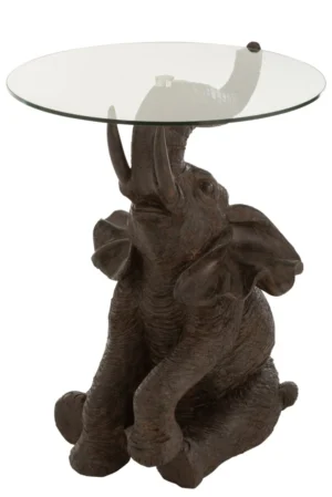 De Bijzettafel Bruin 63 CM Glas is een glazen bijzettafel met een donkerbruine olifantenvoet met textuur, waarvan de slurf omhoog staat om het ronde glazen oppervlak te ondersteunen.