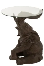 De Bijzettafel Bruin 63 CM Glas is een bijzettafel in de vorm van een bruine olifant die rechtop zit en met zijn opstaande slurf een rond tafelblad van helder glas ondersteunt.
