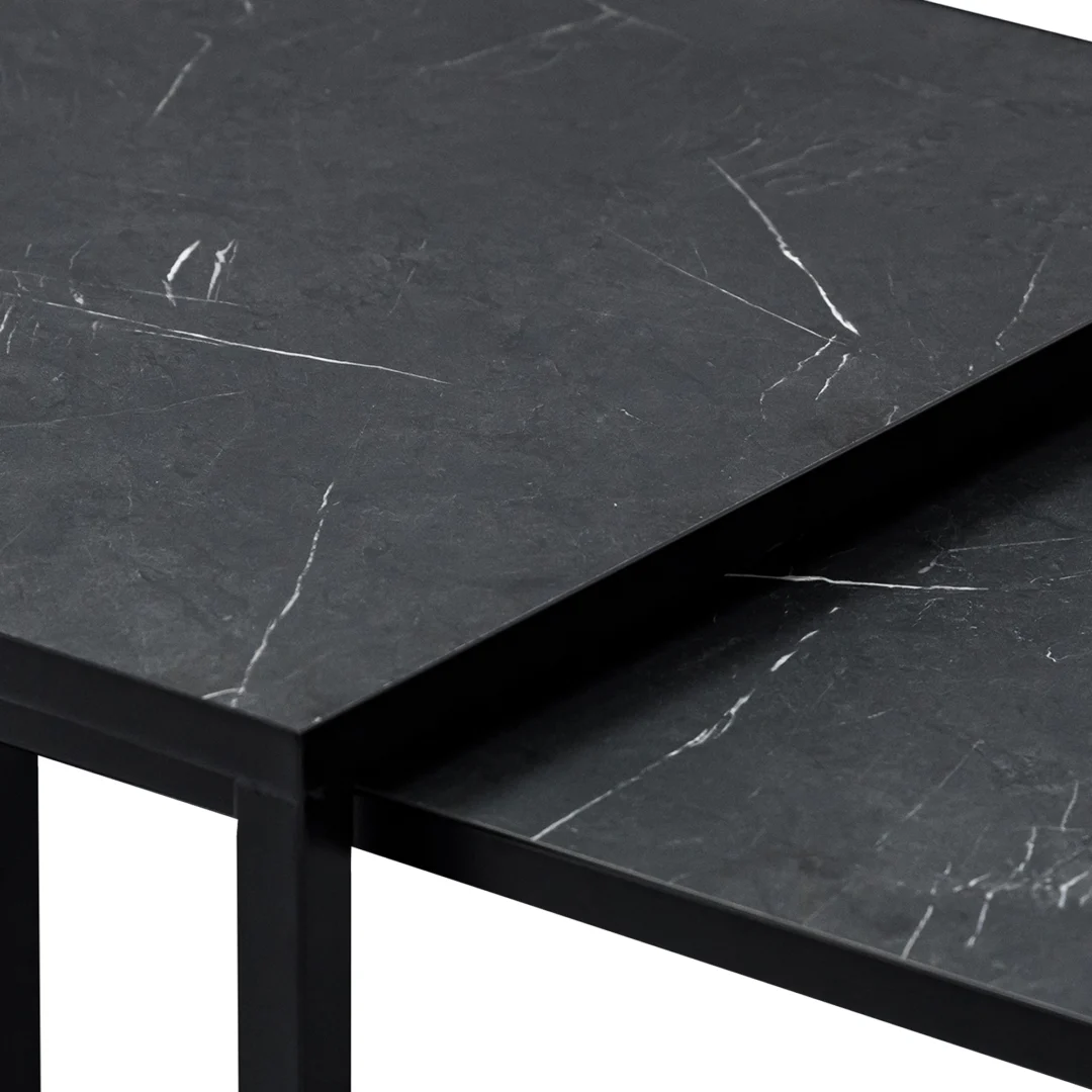 De Salontafel Zwart 67 x 44 CM Marmer bestaat uit twee zwarte nesttafels met een matte, marmerachtige afwerking en witte adering. De kleinere tafel schuift onder de grotere, wat de moderne, minimalistische stijl benadrukt.